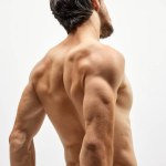 Strength, power and beauty. Back view of strong musculed young man posing topless over white background. Beauty, fashion, sport, fitness and body care concept