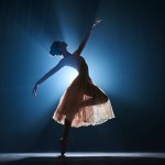 Attractive, artistic, talented young girl, ballerina dancing classical dance, performing against dark blue background with spotlight. Concept of art, classical ballet, creativity, choreography, beauty