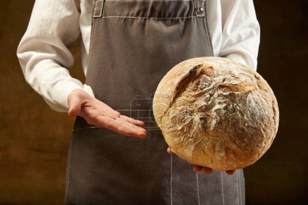 Téléchargez les photos : Baker tient du pain au levain maison fraîchement cuit. Concept d'alimentation, santé, traditions, boulangerie et publicité - en image libre de droit