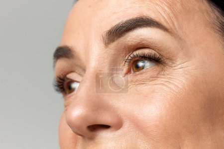 Photo for Cropped portrait of beautiful middle-aged woman with healthy, natural condition skin looking away over grey studio background. Fashion, beauty, spa, cosmetology, skin care concept. - Royalty Free Image