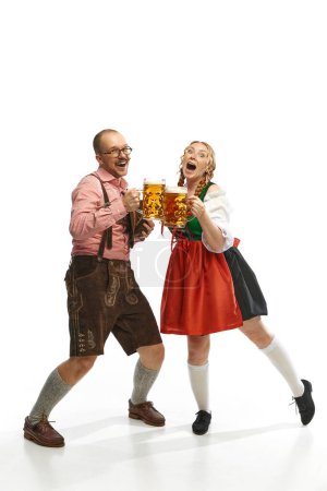 Photo for Two cheerful friends. Full lenght portrait of emotional man and woman wearing folk festival outfits with Bavarian beer glasses. Concept of alcohol, traditions, holidays, festival. Copy space for ad - Royalty Free Image