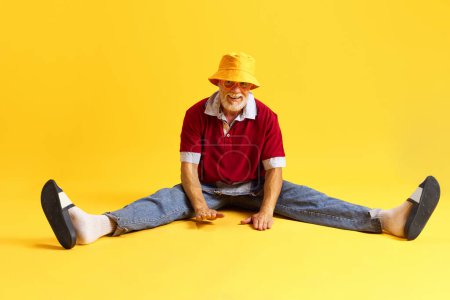 Full length body size view of attractive cheerful funny man dressed denim outfit sitting on floor and having fun isolated bright yellow background. Concept of dashion, style, emotions, holiday. Ad.