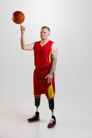 Photo for Attractive, confident, sporty man with prosthetic legs, disability in uniform spins basketball ball on finger. Sport for people with disabilities. concept of sport, player, medical, health, body care. - Royalty Free Image