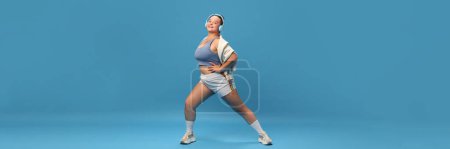 Photo for Self-care and well being. Young smiling plus-size woman doing exercises lunges in sportswear against blue studio background. Motivation. Concept of sport, body-positivity, weight loss. Banner - Royalty Free Image