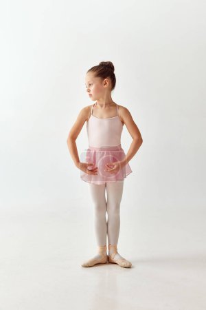Téléchargez les photos : Portrait de petite danseuse de ballerine préscolaire adorable en robe de ballet tutu rose et en pointe legging blanc debout posant sur fond blanc. Concept de beauté, mode, passe-temps, expression de soi - en image libre de droit