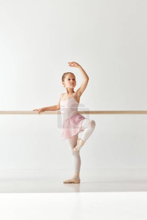 Photo for Rear view portrait of small adorable ballerina dancer girl in rose tutu ballet dress on pointe posing and performing dance elements in studio, dance school. Concept of beauty, fashion, hobby, action. - Royalty Free Image