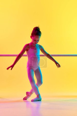 Téléchargez les photos : Portrait de petite fille danseuse de ballerine enfant délicate sur pointes posant près de barre dans la lumière néon mixte. Genre développement de la personnalité. Concept d'art, de beauté, de mode, de passe-temps, d'action. publicité - en image libre de droit