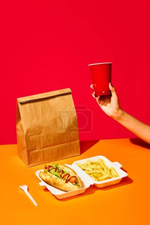 Photo for Packing food boxed take away. Tasty hotdog with hot sausage served mustard and ketchup and green salad with fried potato and drink against vivid red background. Concept of fast food, menu, catering. - Royalty Free Image