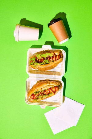 Photo for Top view of hot tasty American hotdogs with sausages in mustard and ketchup with green salad and paper cups against green background. Concept of fast food, street food, delivery. Copy space for text - Royalty Free Image