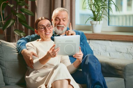 Photo for Happy cheerful young couple sitting in living room no couch with tablet and relaxing while watching movie. Weekend. Concept of love, retirement life, pensioners, cozy, winter holidays. - Royalty Free Image