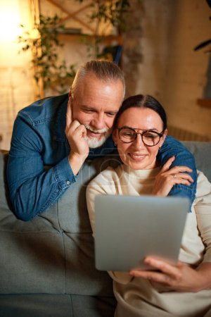 Photo for Lovely, elderly people, mature couple relaxing on sofa in living room and using digital tablet for video call or networking. Concept of love, retirement life, pensioners, winter holidays, technology. - Royalty Free Image