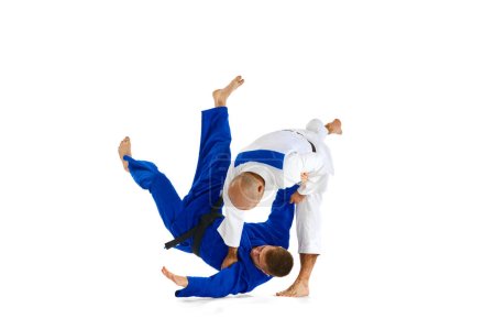 Téléchargez les photos : Deux jeunes hommes judoistes professionnels combattant, effectuant des compétences techniques isolé fond studio blanc. Concept d'art martial, sport de combat, santé, force, énergie, forme physique. Espace de copie - en image libre de droit