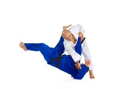 Téléchargez les photos : Deux combattants de karaté caucasiens en kimono blanc et bleu avec des ceintures noires exécutant des compétences en action isolé fond blanc. Concept d'art martial, sport de combat, force, énergie, ajustement. Espace de copie - en image libre de droit