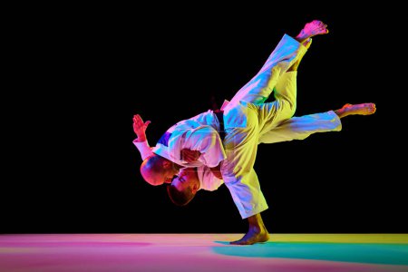 Photo for Portrait of two athletic, strong men, professional judokas, fighters showing their skills in neon light while competition isolated black background. Concept of martial art, combat sport, energy, fit. - Royalty Free Image