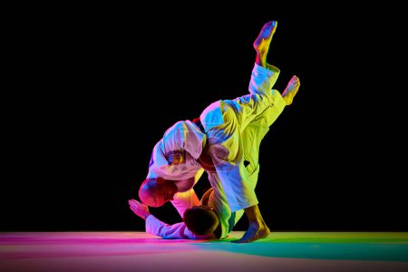 Photo for Two athletic, strong men, professional judokas, fighters showing their skills while competition in mixed neon light isolated black background. Concept of martial art, combat sport, health, energy. Ad - Royalty Free Image