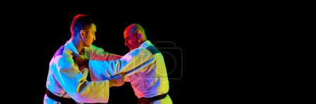 Photo for Banner. Portrait of two man looking eyes to eye while fighting in neon light isolated black background with negative space to insert your text. Concept of martial art, combat sport, health, energy. - Royalty Free Image