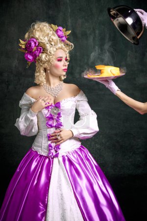 Photo for Portrait of attractive woman in old-fashion, renaissance dress and hairstyle and waiter serving dinner toy-chicken against vintage background. Concept of food, catering, restaurant menu, delivery. - Royalty Free Image