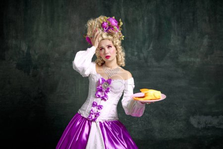 Photo for Upset, dissatisfied with plastic dinner woman, in old fashioned renaissance dress and hairstyle decorated flowers over vintage background. Concept of nutrition, catering, restaurant menu, delivery. - Royalty Free Image
