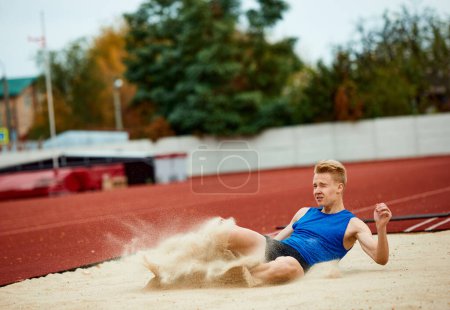 Photo for Athletic prowess on display: man mid-flight in long jump. Professional, skilled sportsman landing in sand court of impressive long jump Concept of kinds of sport, championship, motivation, energy. - Royalty Free Image
