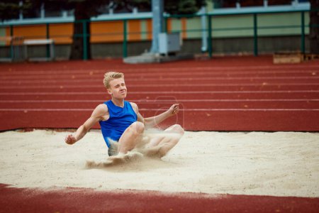 Photo for Photography highlights dynamic arc of long jump in exquisite detail. Professional, skilled sportsman landing in sand court of impressive long jump Concept of kinds of sport, championship, motivation. - Royalty Free Image