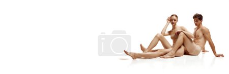 Foto de Banner. Atractiva pareja desnuda sentada en el suelo y posando sobre fondo blanco estudio con espacio negativo para insertar texto. Concepto de belleza, amor, cuidado corporal, productos cosméticos, moda. - Imagen libre de derechos