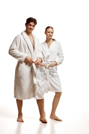 Photo for Full length portrait of young couple, man and woman posing in bathrobes against white studio background. Concept of natural beauty, spa resort, salon, treatment, relationship, love, hygiene. - Royalty Free Image