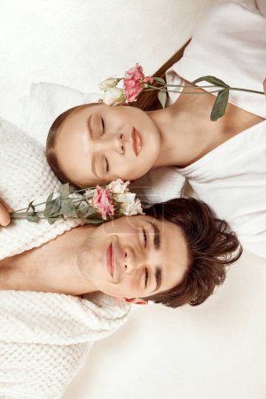 Photo for Close up top view portrait of couple, man and woman lying with clothed eyes and flowers against white studio background. Concept of beauty, spa resort, relationship, love, selfcare treatment. - Royalty Free Image