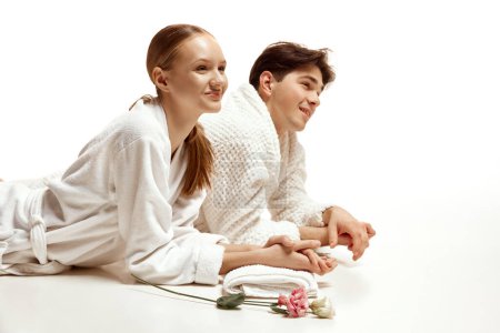 Photo for Close up portrait of couple, man and woman in bathrobe having spa procedures in salon with flowers against white studio background. Concept of beauty, resort, relationship, love, selfcare treatment. - Royalty Free Image