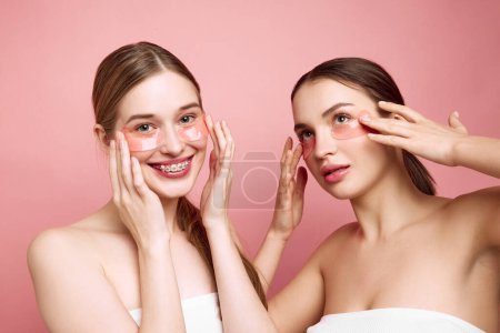 Photo for Radiant Rituals. Portrait of two young attractive girls applying under-eye moisturized patches. Girls embrace natural beauty. Concept of beauty treatments, morning routine, anti-aging, spa. - Royalty Free Image