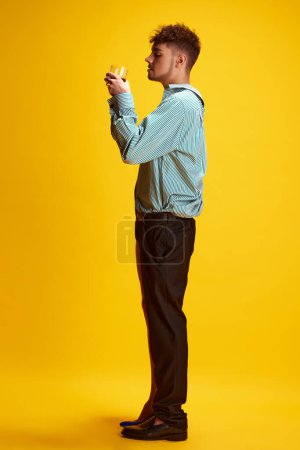 Foto de Retrato de vista lateral de modelo masculino vestido como hombre y mujer en unidad bebiendo alcohol disparado contra fondo amarillo del estudio. Concepto de auto-expresión, moda y estilo, belleza, estilo de vida. Anuncio - Imagen libre de derechos