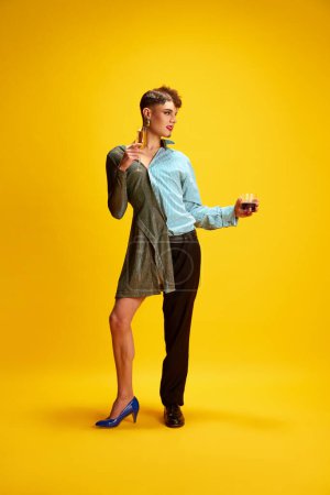 Photo for Model elegantly half-dressed in dress and smart casual costume, holds glasses of whiskey and champagne, breaking gender stereotypes and encouraging self-expression. Concept of fashion and style. - Royalty Free Image