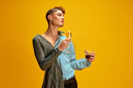 Photo for Overjoyed man with womans and mans appearance holding glasses with alcohol drinks against vivid yellow background. Concept of self-expression, fashion and style, beauty, lifestyle. Ad - Royalty Free Image