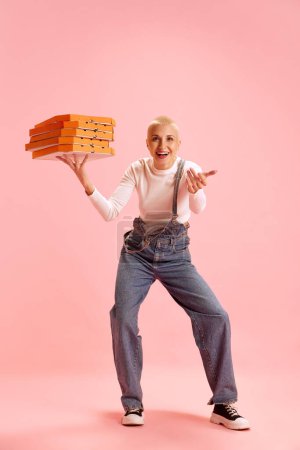 Portrait complet de jeune femme attirante regardant la caméra et tenant une énorme pile de boîtes avec pizza. Concept de restauration rapide, traiteur, mode et tendances, livraison.