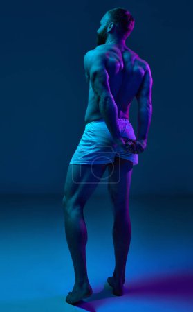 Photo for Full length photo. Rear view of young, fit naked man demonstrated his perfect and healthy back shape in neon light against gradient background. Concept of beauty and fashion, art, aesthetic of body. - Royalty Free Image