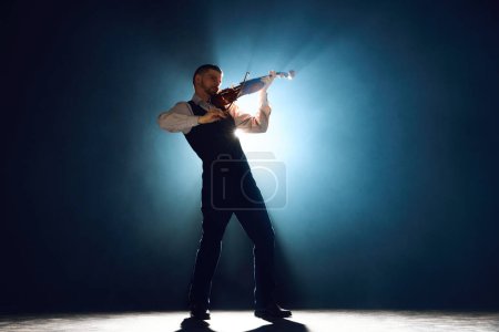 Foto de Músico clásico tocando el violín, tocando la melodía en el escenario con el foco detrás de él rodeado de humo. Concepto de festivales de música instrumental y conciertos, arte, cultura. Anuncio - Imagen libre de derechos