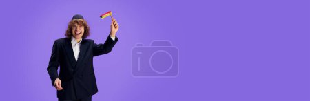Photo for Jewish man with grogger posing against purple against purple studio background with negative space to insert text. Purim, business, festival, holiday, celebration Pesach or Passover, Judaism concept. - Royalty Free Image
