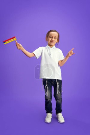 Little Jewish boy, kid playing with grogger against purple studio background. Celebration of Purim, national Jewish holiday. Festival, Pesach or Passover, Judaism, religion concept.