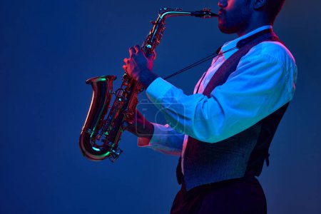 Téléchargez les photos : Musicien de jazz afro-américain jouant du saxophone ses mélodies majeures sur fond bleu dans un éclairage mixte rose-violet. Concept d'instrument de musique classique, concerts et festivals. Publicité - en image libre de droit