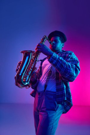 Téléchargez les photos : Musicien de jazz en tenue rétro jouant vertueusement du saxophone sur fond dégradé bleu-rose au néon. Concept de blues, musique instrumentale chic, festivals et concerts. Publicité - en image libre de droit