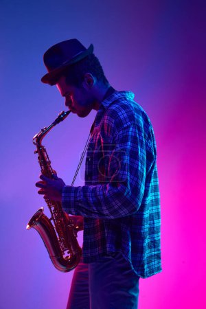 Téléchargez les photos : Portrait de saxophoniste solo talentueux jouant pièce sur fond dégradé rose-bleu dans la lumière néon. Concept de jazz, blues, musique instrumentale chic, festivals et concerts. Publicité - en image libre de droit