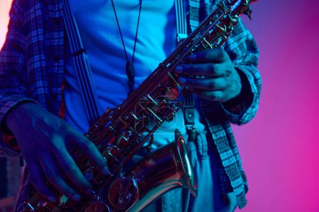 Téléchargez les photos : Portrait recadré de jazzman tenant un saxophone sur fond bleu-rose dégradé sous la lumière néon. Des mélodies jazz. Concept de jazz, blues, musique instrumentale chic, festivals et concerts. Publicité - en image libre de droit