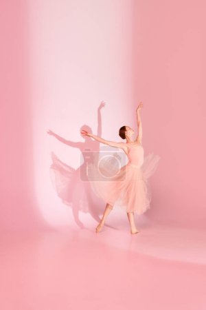 Photo for Graceful Ballet. Young woman, classic ballerina dancing barefoot in pink dress against pastel studio background with her shadow. Concept of elegance, ballet, beauty, motion and action. - Royalty Free Image