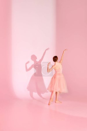 Photo for Balletic Grace. Classic ballerina dances barefoot in pink swimsuit and long skirt against pastel pink background with her shadow. Concept of elegance, femininity ballet, beauty, dance school. Ad - Royalty Free Image