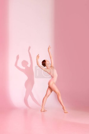 Photo for Whispering Grace. Ballerina in pink attire dancing against soft background, her shadow mimicking her every move. Concept of art and ballet, grace and beauty, fluidity, shadow dance. - Royalty Free Image