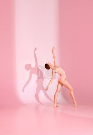Photo for Blush Ballet. Young woman, ballerina, dancer in pink attire poses against pastel studio backdrop. Her shadow dances alongside her. Concept of ballet, beauty, elegance, shadowplay, harmony. - Royalty Free Image