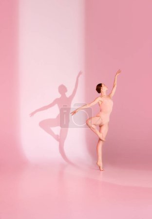 Photo for Pastel Pirouette. Young woman, ballerina dancer in pink ensemble poses against soft background. Her shadow dances in tandem. Concept of ballet, grace, beauty, harmony, shadowplay. Ad - Royalty Free Image