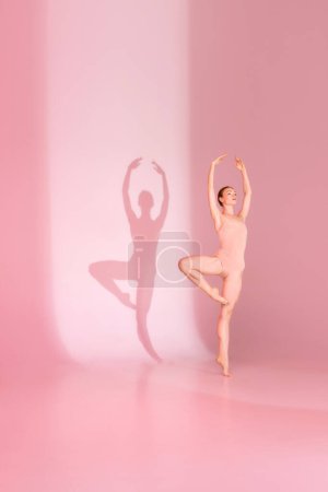 Photo for En Pointe in Pink. Ballerina, dressed in athletic gear, poses against muted palette. Her shadow mirrors her elegance. Concept of art, ballet, grace and beauty, poise, shadow dance. - Royalty Free Image