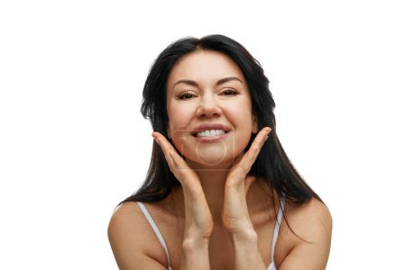 Portrait of cheerful woman with hands touching chin, looking at camera against white studio background. Concept of beauty and fashion, spa treatments, self care, body care, wellness. Ad