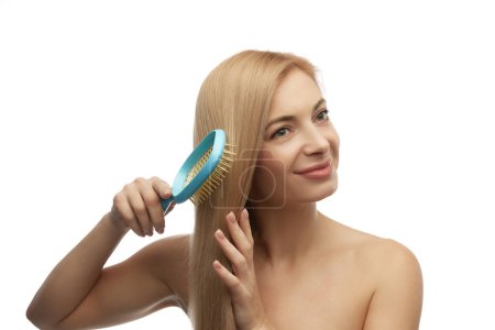 Young attractive woman combing blonde, healthy and silky hair against white studio background. Beauty and health of hair Concept of natural beauty, spa, cosmetology, female health, hair care. Ad