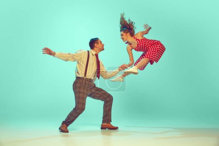 Dynamic shot of energetic swing dance scene, couple performing in motion against gradient mint background. Retro fashion. Concept of jazz, comparisons of eras, music, energy, happiness, mood, action